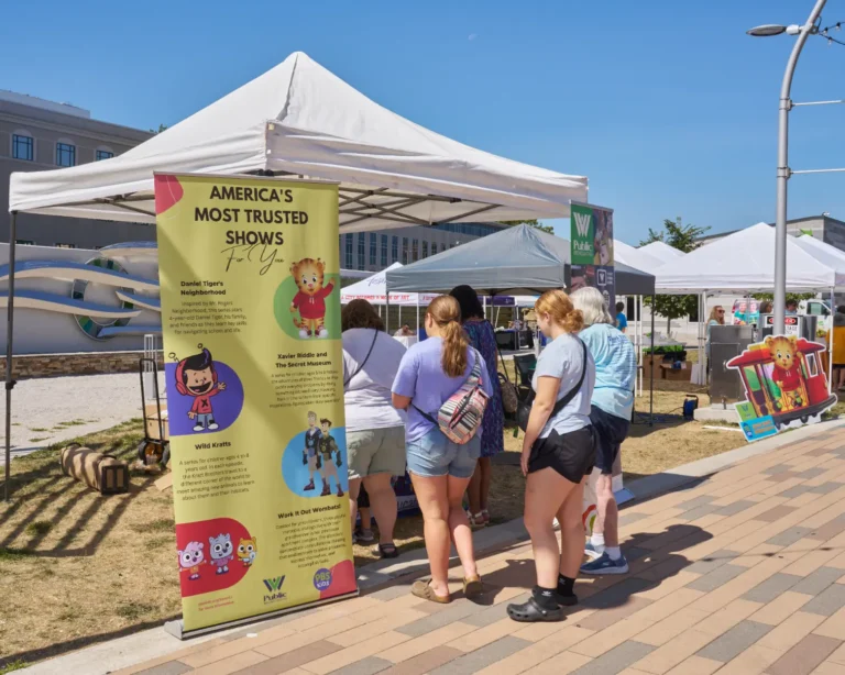 Several people stand farther away from the camera. Several vendor tables are visible.