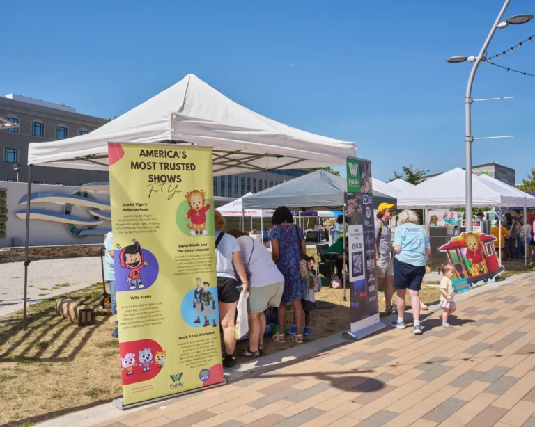 Several people stand farther away from the camera. Several vendor tables are visible.
