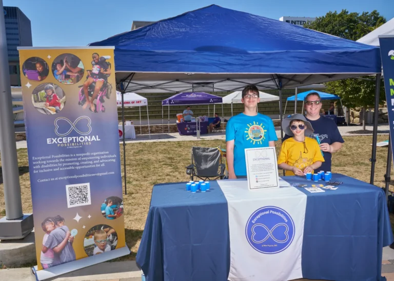 Three people stand behind a vendor table. The popup banner next to the table says, Exceptional Possibilities.