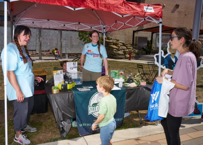 Three adults and one child. The stand around a vendor table and are chatting.