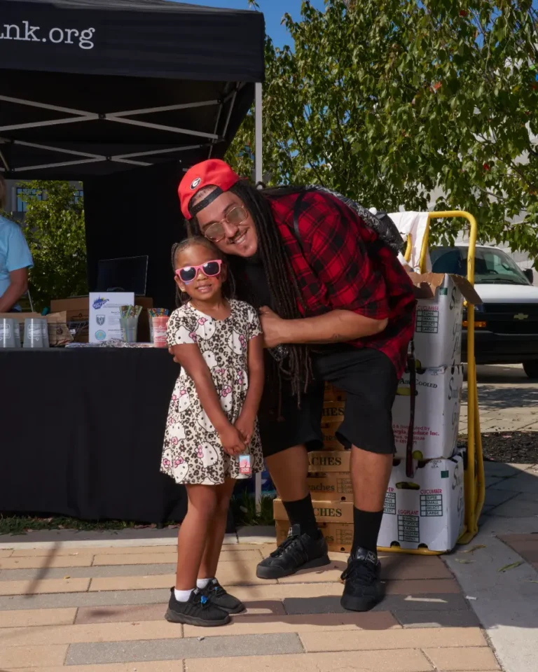 A man leans down to pose for a photo with a young girl. They both smile.