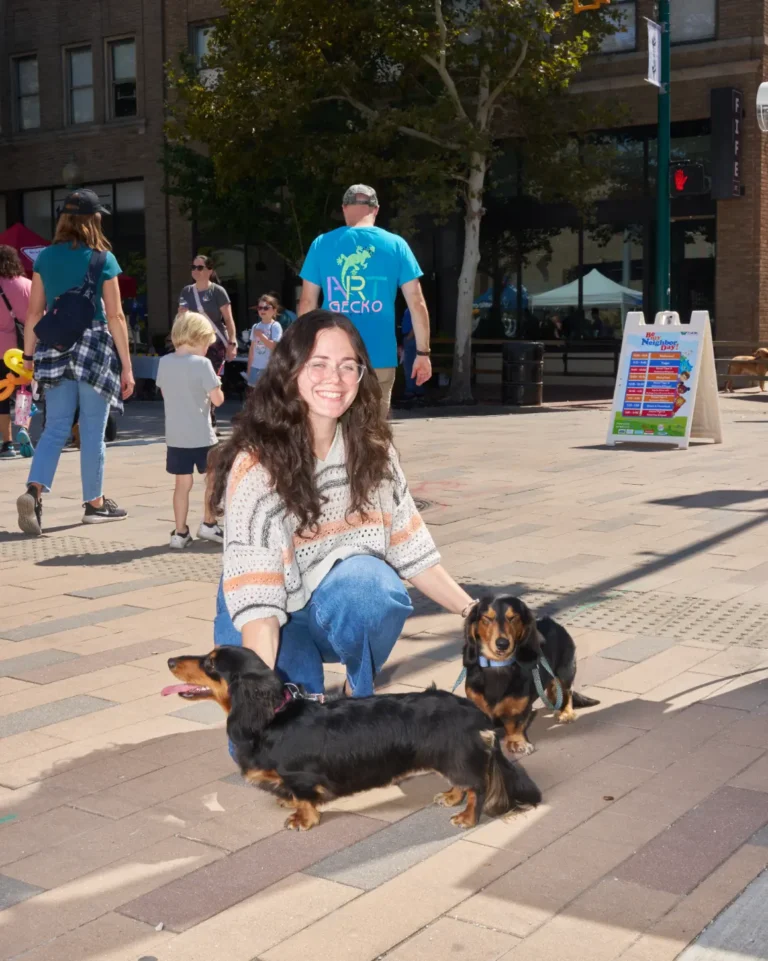 A woman with two dachshunds. The woman is wearing glasses and smiling toward the camera.