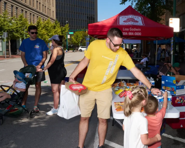 A man picks up water bottles off a table. Two children are seen next to him.