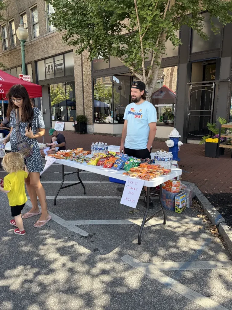 A man stands behind a table offering free food and drinks.
