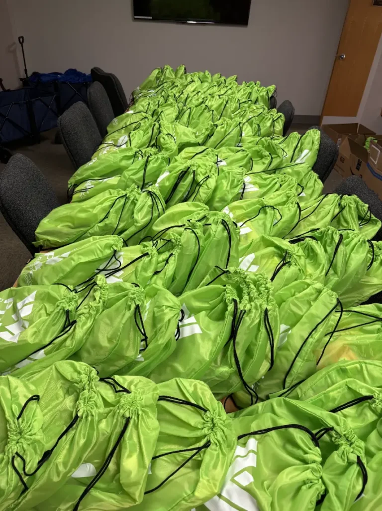 Dozens of green bags full of goodies are shown on a table.