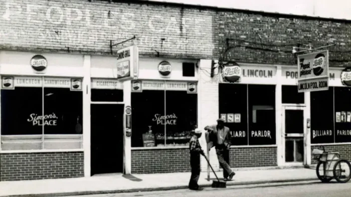 A black and white photo of two Black men standing outside a store. 