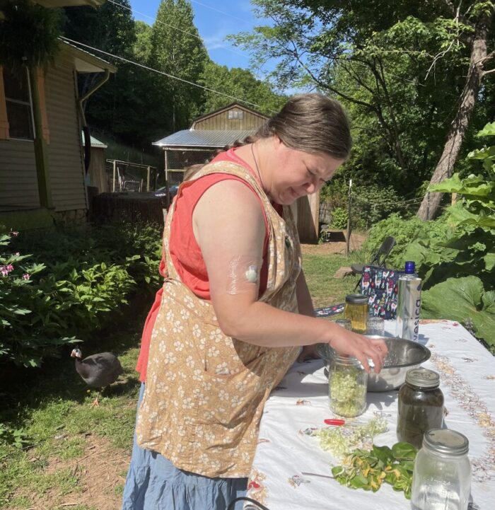 A white woman filling mason jars with herbs. She is standing outside at a table. 