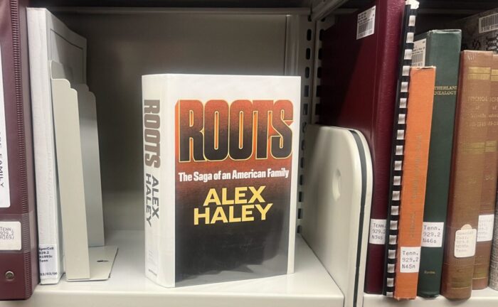 A book sitting on a bookshelf. The title on the cover of the book is "Roots" by Alex Haley.
