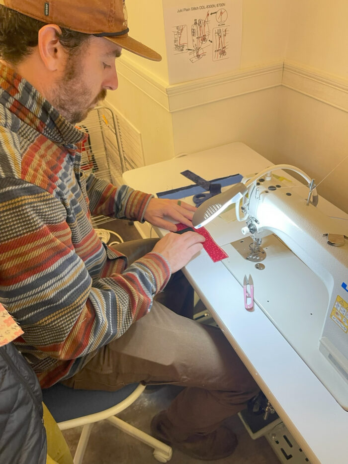 A man sews scraps of material with a sewing machine.