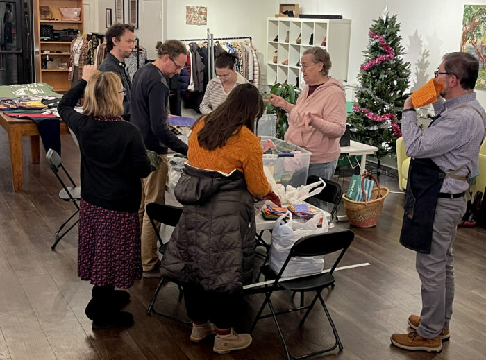 Half a dozen people stand around a table covered in scraps of material