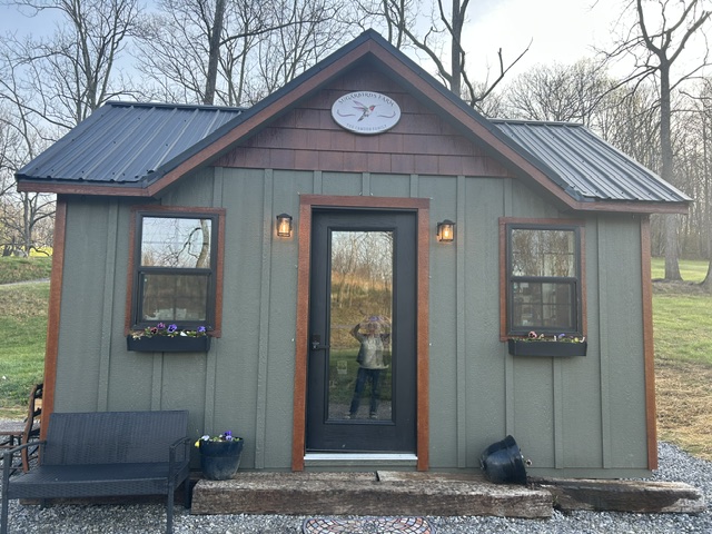 The exterior of a green building. There are two windows and a glass front door. 