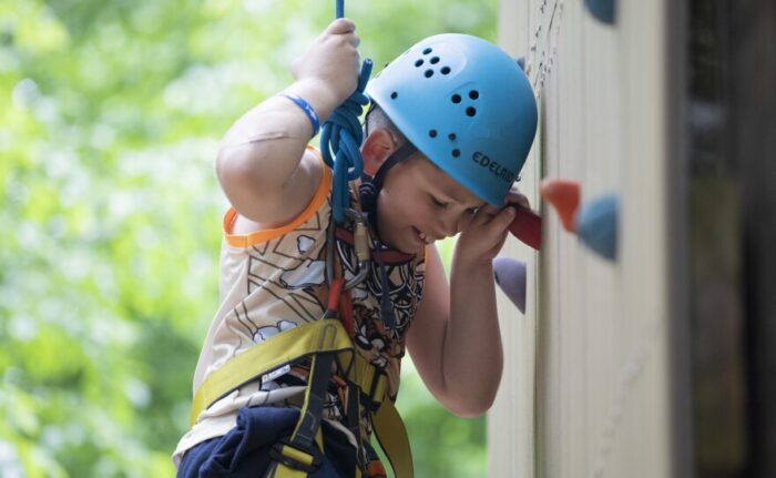 A young white boy wearing a blue helmet. He is climbing a rock wall.