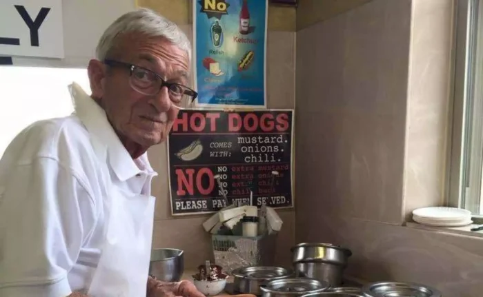 A photo of an older white man making hotdogs. 