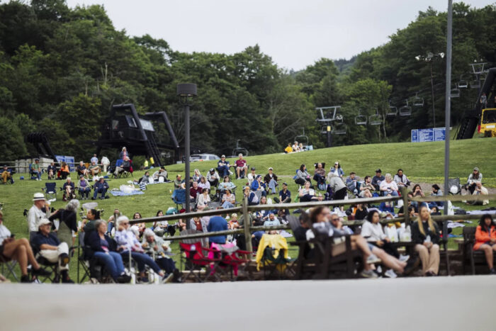 Group of people sit in lawn chairs at a park with ski lifts in the background