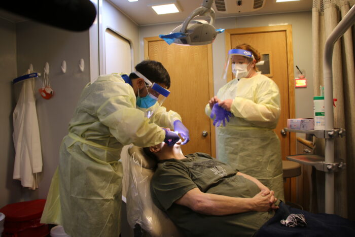 Patient in a dental chair with two clinicians in yellow gowns