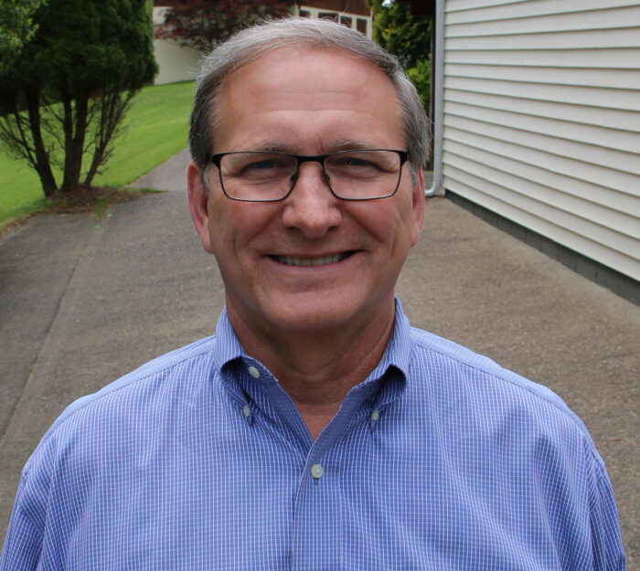 Man in blue checked shirt smiles into camera