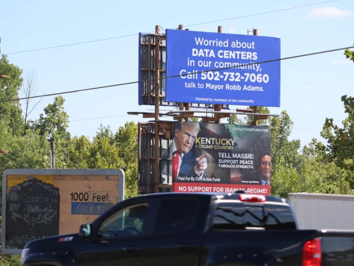 Two billboards stacked on top of each other. The one on top is blue with the words "Worried about data centers in our community? Call 502-732-7060. Talk to Mayor Rob Adams. Below the blue billboard is one featuring President Donald Trump and reads, "Kentucky = Trump Country."