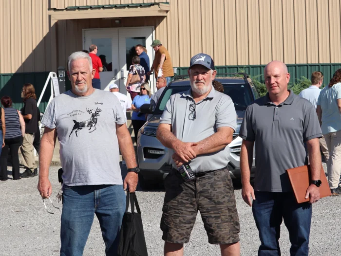 Three men pose for a photo, not smiling. It is a sunny day.