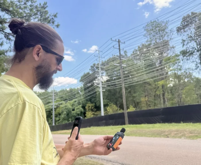 A man stands near a fence while holding a noise level device.