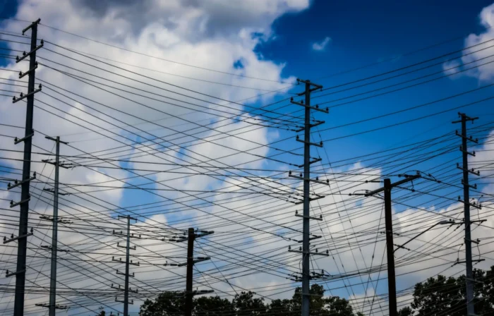 Power lines are seen from the ground. They are seen against a blue, cloudy sky.