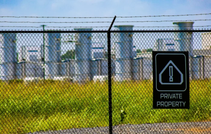 Outside a fence that has a sign posted that reads "private property." In the distance, beyond the fence are several gas turbines.
