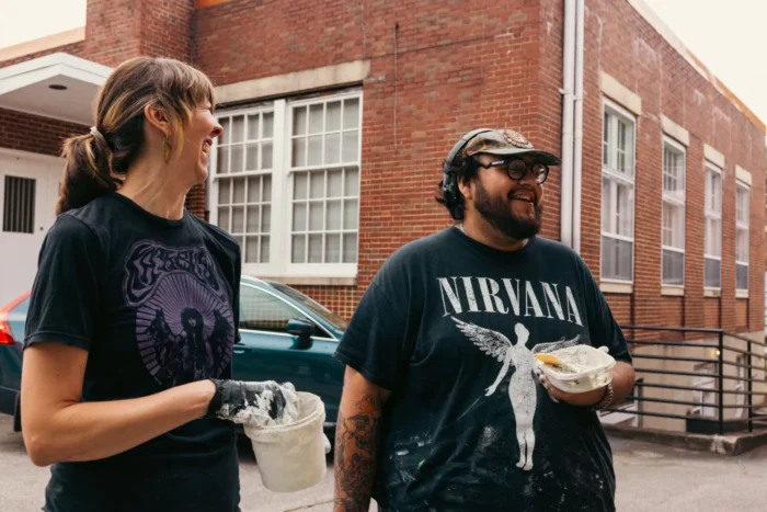 A landscape photo of two people holding mosaic materials. 