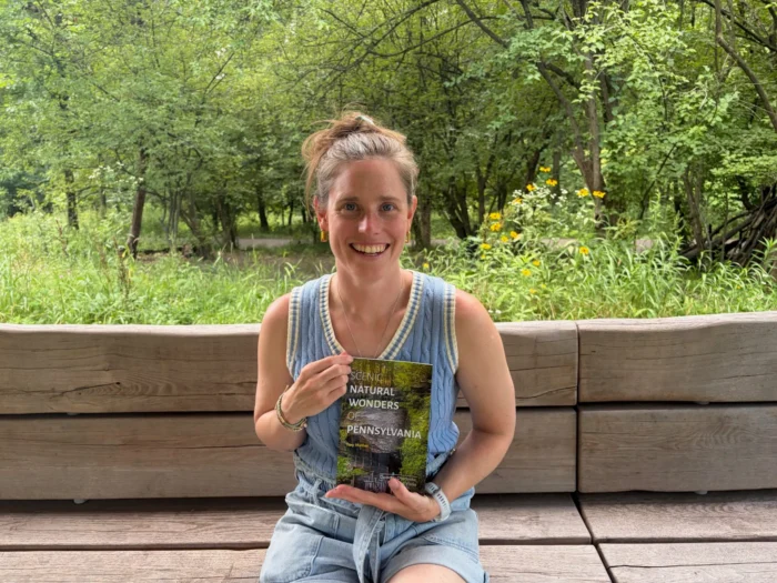 A white woman sitting on a bench and holding a book. 