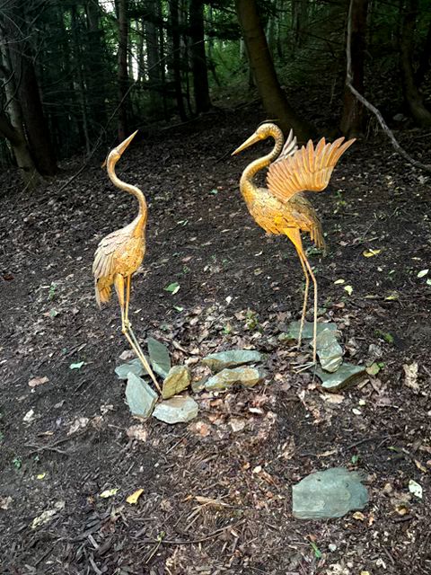 Two golden crane statues standing in a garden. 