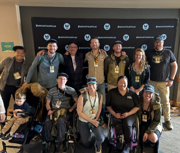Two rows of people standing, squatting and sitting in front of a backdrop that reads, "Mountainfilm."