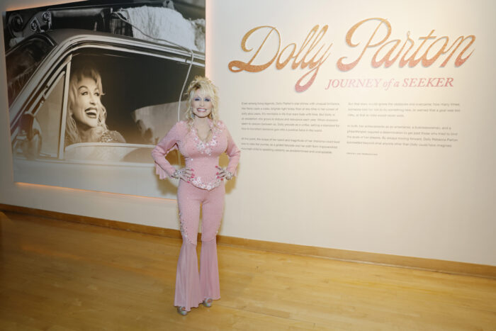 A white woman standing in front of a sign that says "Dolly Parton: Journey of a Seeker."