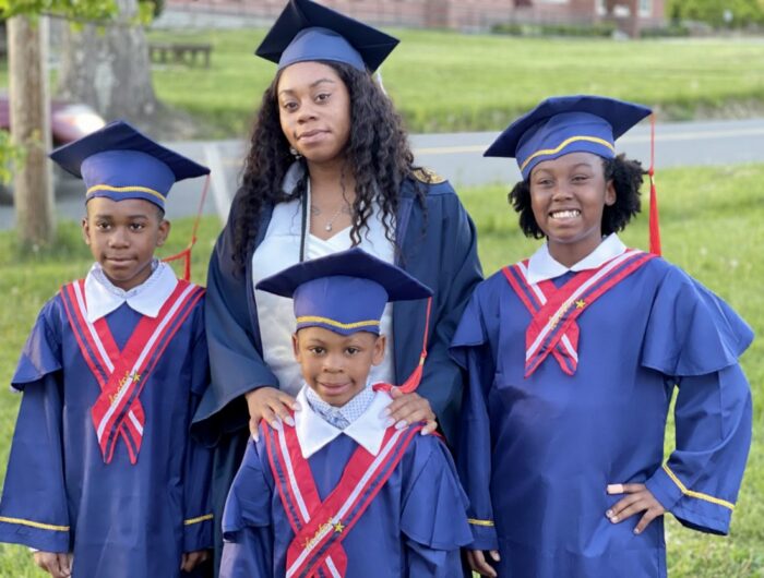 A family of four. One adult woman and three children. They are dressed as if they are attending a graduation. They are standing outside.