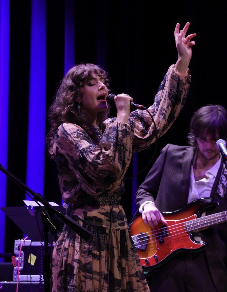 woman sings into mic with her hand in the air