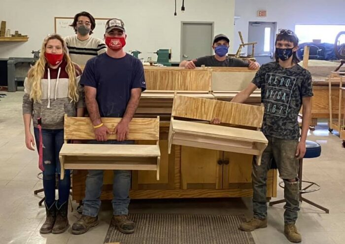 A group photo of five young people wearing masks and holding wood pieces that have been formed to look like small benches.