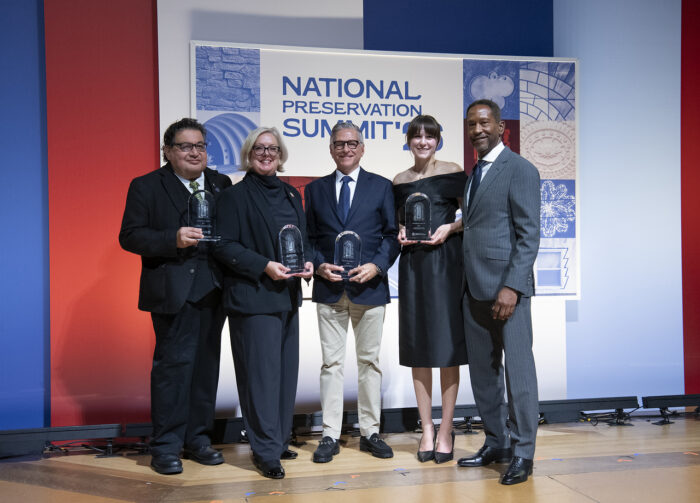 A row of five people stand holding glass awards in front of a backdrop branded "National Trust for Historic Preservation"