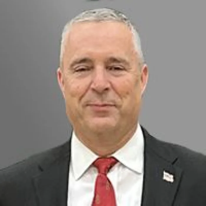 A professional photo of an older man. He wears a suit and tie.