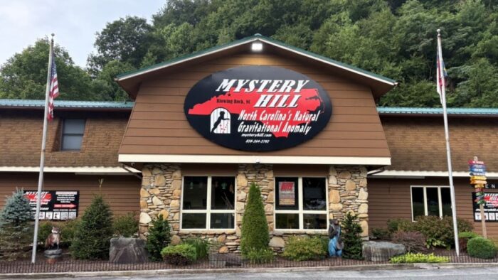 The exterior of a brown building. There is a red and black sign on the front that reads, "Mystery Hill."