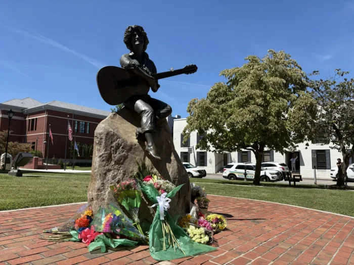 A statue of Dolly Parton with flowers at the base of the statue. 