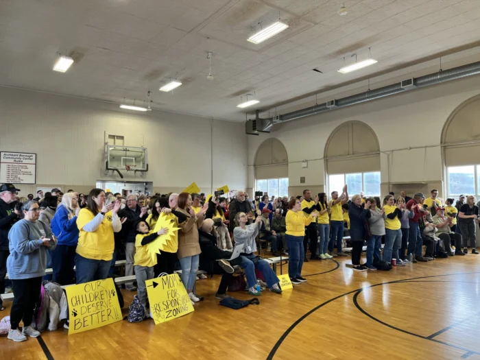 A landscape photo of a room full of people wearing yellow. They are in a gymnasium and are holding signs. 