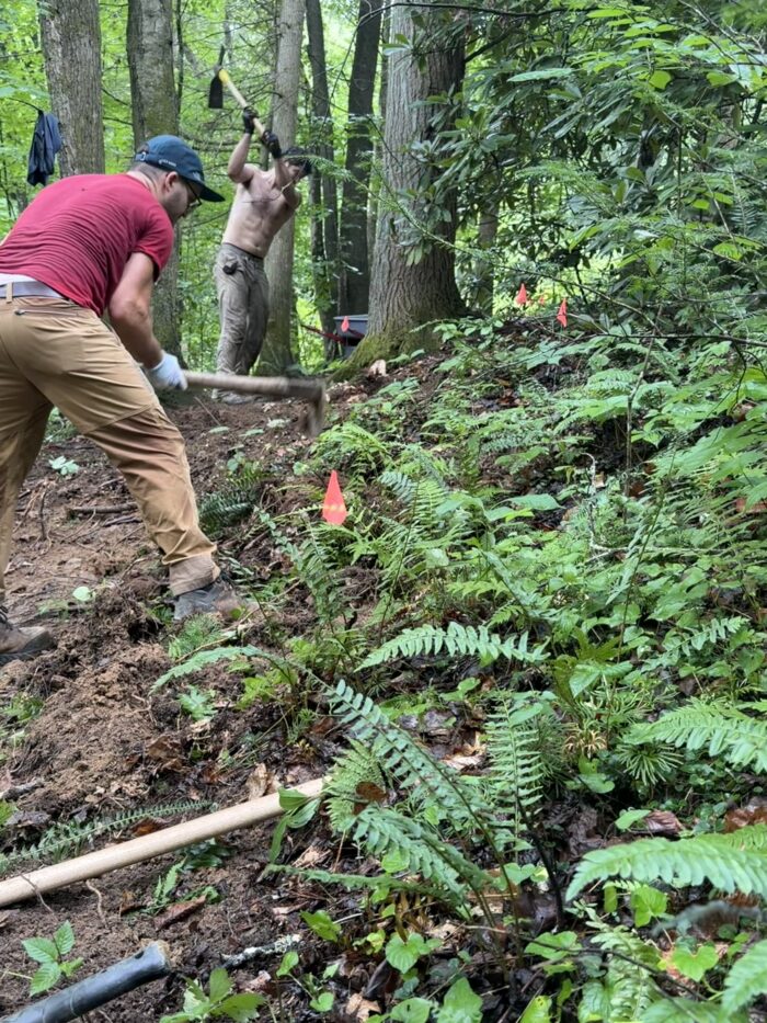 Two people are shown widening a trail with pickaxes.