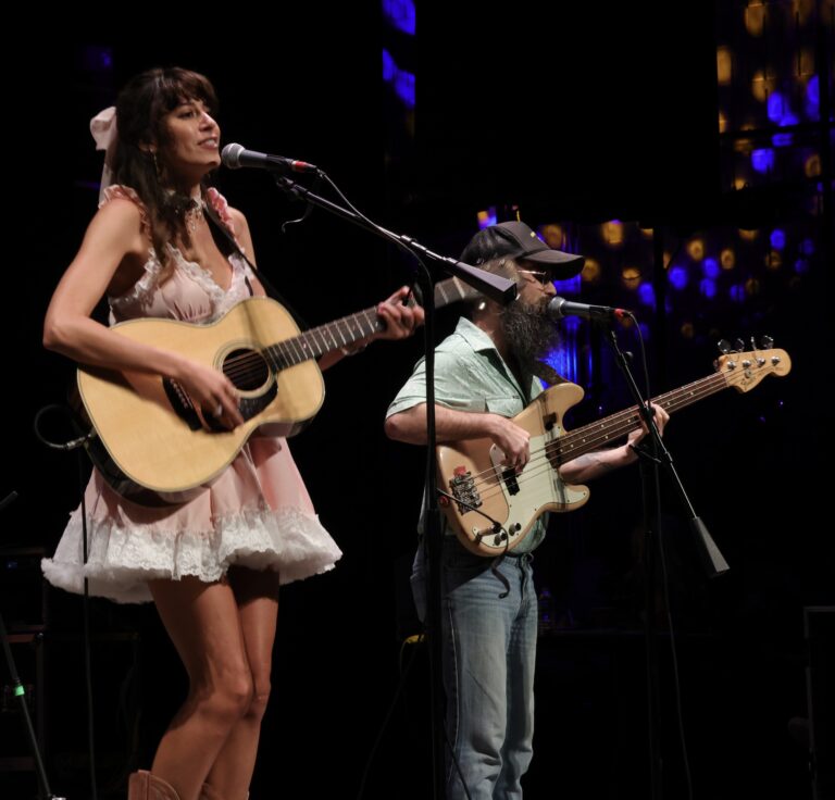 woman playing guitar sings into mic