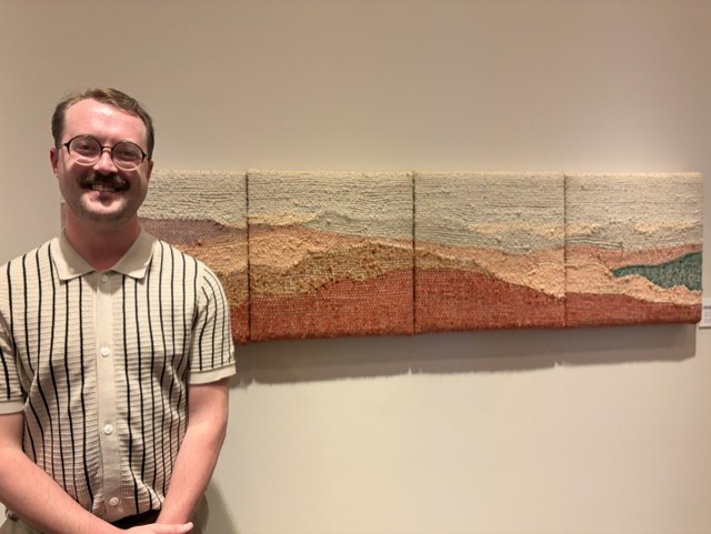 A landscape portrait of a white man standing in front of a weaved landscape. 
