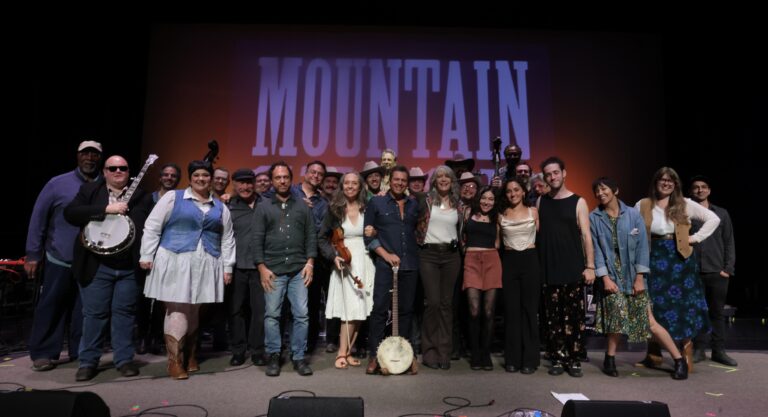 large group of musicians pose on stage with Kathy Mattea