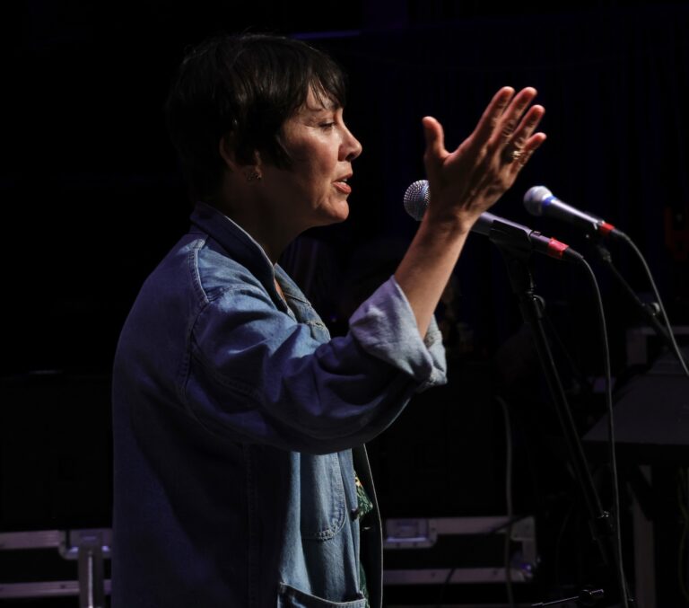 a woman sings into mic with her hands in the air