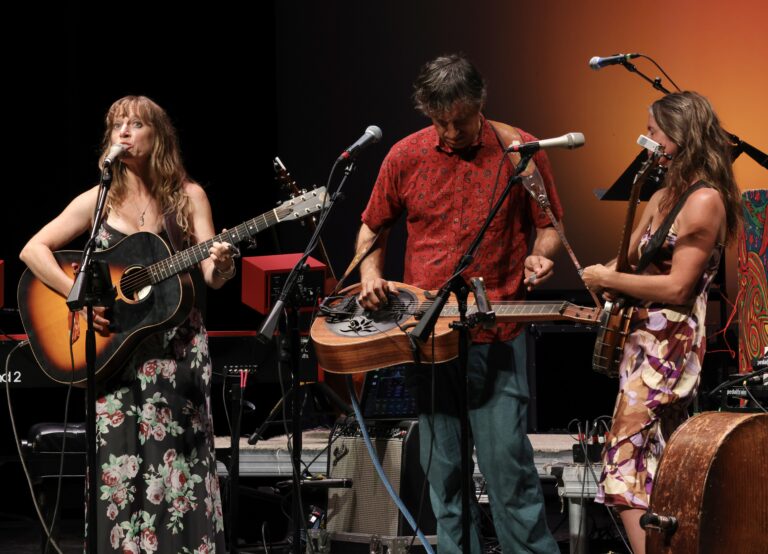 Three musicians play instruments on stage