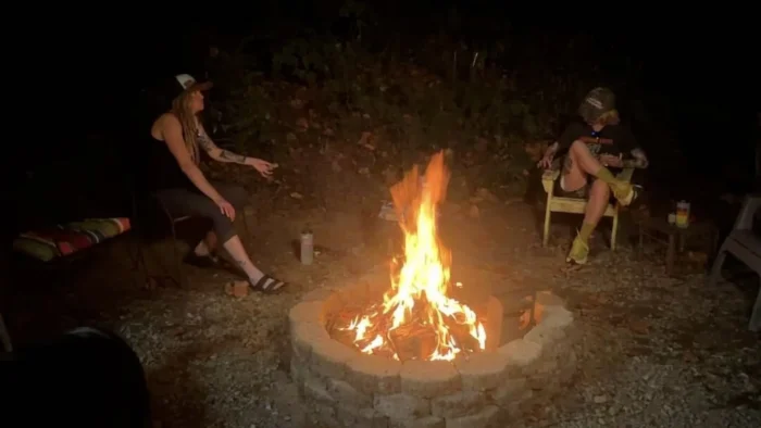 Two women sit around a fire at night.