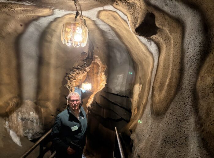 A white man standing in a cave tavern. There is a lantern hovering above him.