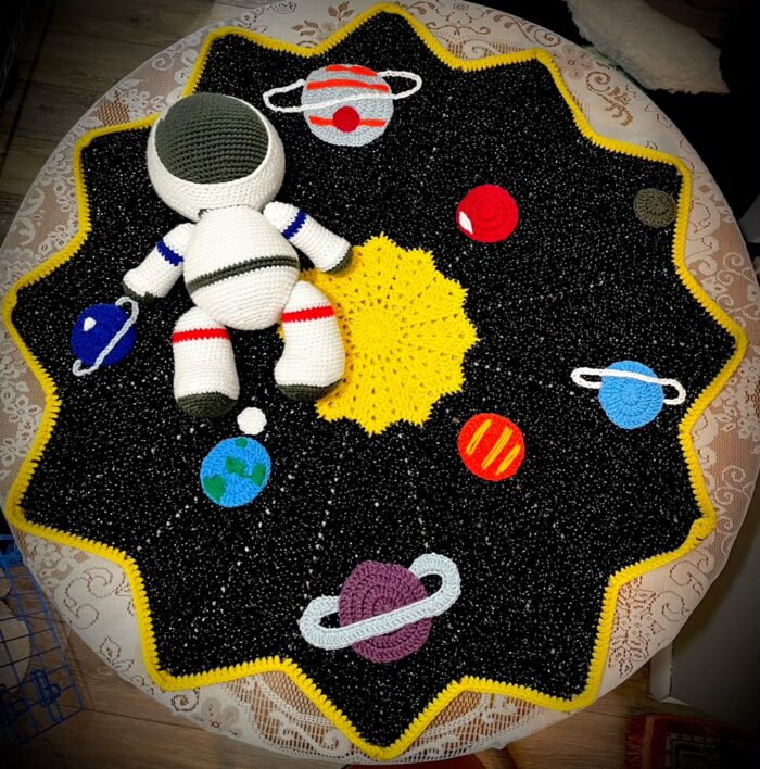 A photo of a crocheted galaxy. There is a sun, several planets and a crocheted astronaut plushie.