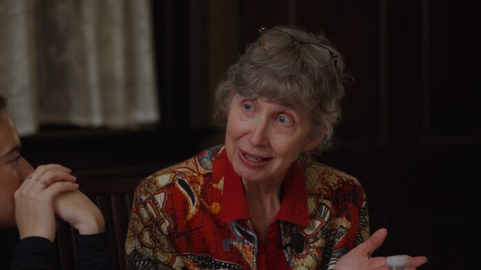 An older woman wearing a red shirt and sitting at a dinner table.