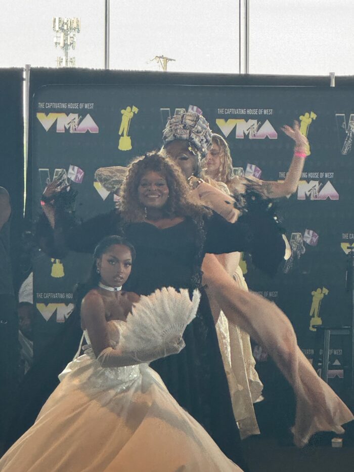 Four women pose and smile for the camera, dressed in extravagant outfits.