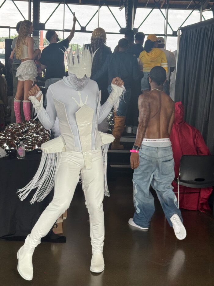 A person dressed in full white and appearing like a snow queen perhaps is dancing. They are surrounded by several other people dressed up.
